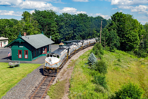 Cresco, United States - July 19, 2016: Five Delaware-Lackawanna Railroad locomotives drag a heavy grain train past the small, neat railway station building at Cresco on way to Pocono mill.