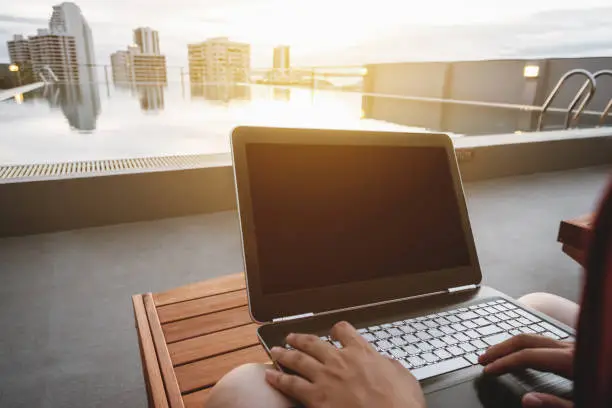 a man using computer laptop, on sunbathe lounge chair at swimming pool in the city, with bright sunlight. Clipping path computer screen