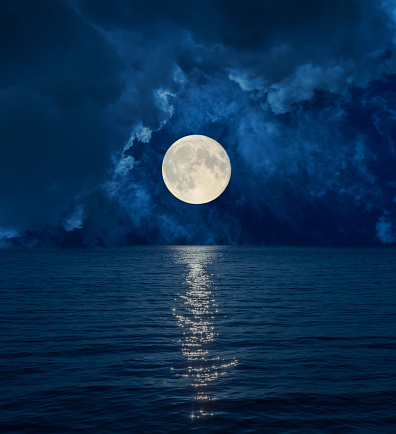 full moon in dark clouds over sea