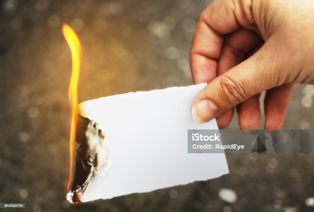 Destroying the evidence: female hand burning paper A woman's hand holds a flaming piece of paper, destroying it and whatever's written on it. Copy space on the unburnt portion of the paper. Paper Stock Photo