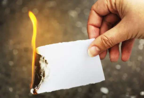 A woman's hand holds a flaming piece of paper, destroying it and whatever's written on it. Copy space on the unburnt portion of the paper.