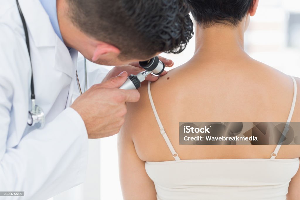 Dermatologist examining mole on back of woman Male dermatologist examining mole on back of woman in clinic Medical Exam Stock Photo