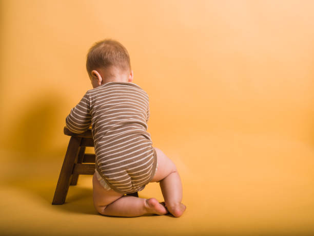 A little baby is learning to stand up using a stool