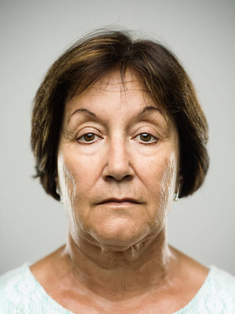 Close up portrait of hispanic mature woman with blank expression against gray background. Vertical shot of real senior woman staring in studio. Short brown hair. Photography from a DSLR camera. Sharp focus on eyes.