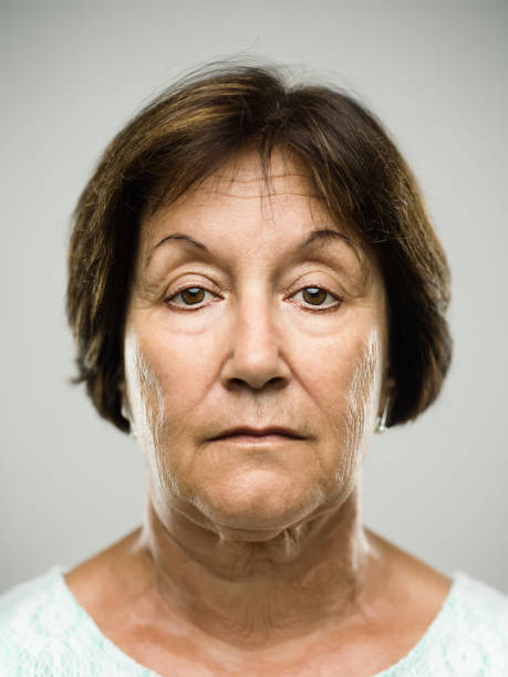 Real serious senior woman portrait Close up portrait of hispanic mature woman with blank expression against gray background. Vertical shot of real senior woman staring in studio. Short brown hair. Photography from a DSLR camera. Sharp focus on eyes. no emotion stock pictures, royalty-free photos & images
