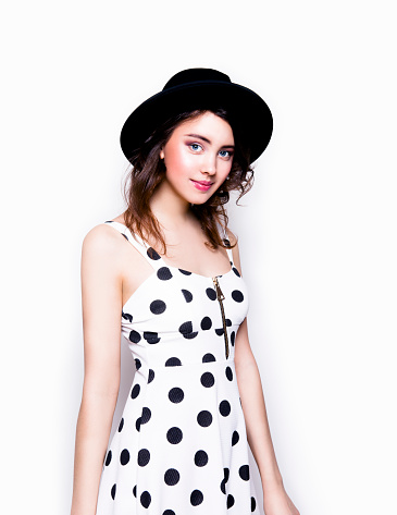 Young beautiful brunette woman with professional make-up looking cute wearing stylish clothes polka dots dress and black hat Fashion model studio portrait on white background