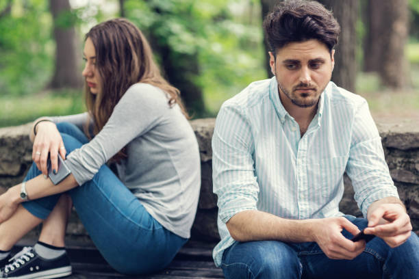 Young couple in relationship difficulties staying away from each other Young sad looking couple sitting at a distance and looking away from each other. Selective focus on the male. couple on bad date stock pictures, royalty-free photos & images