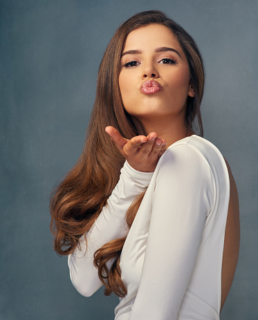 Studio portrait of an attractive young woman blowing a kiss against a grey background