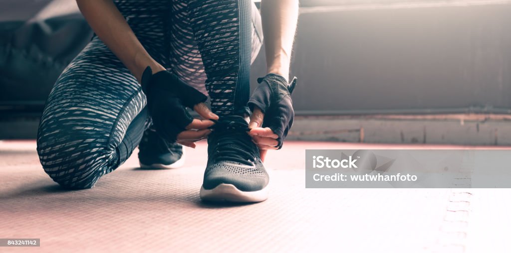 Close up woman sitting with hands lacing up sneakers shoes about healthy lifestyle concept. Cross Training Stock Photo