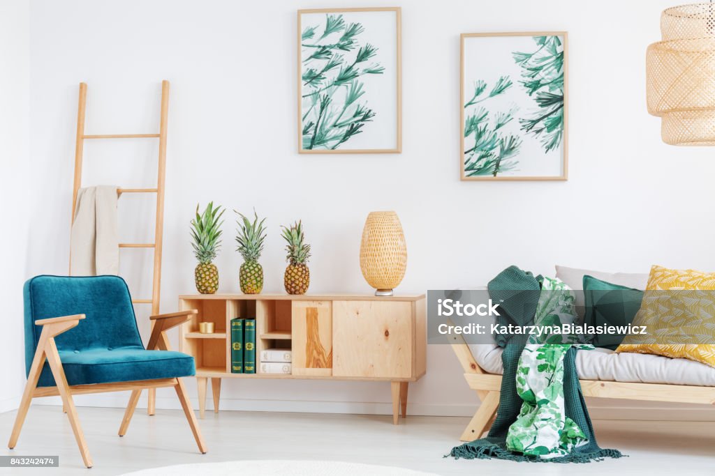 cozy room with pineapples Blue retro chair and yellow pillow on beige sofa in cozy room with pineapples on rustic cupboard Apartment Stock Photo