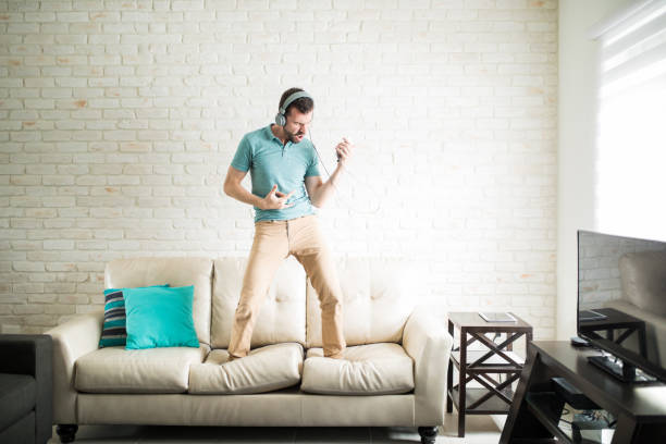 Having fun with an air guitar Modern man listening to music on his phone and standing on the couch playing an air guitar air guitar stock pictures, royalty-free photos & images