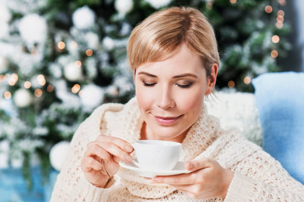 istock Young woman drinking tea by the Christmas tree 843249142
