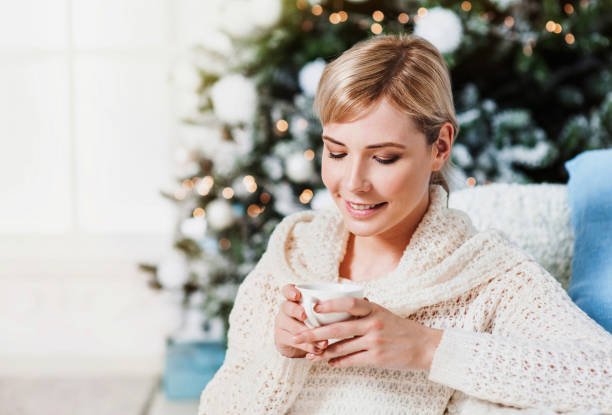 istock Young woman drinking tea by the Christmas tree 843249220