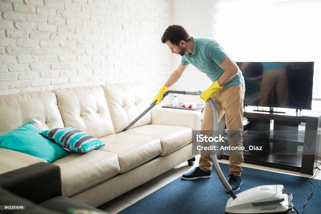 Latin man cleaning the sofa Handsome Hispanic man using a vacuum cleaner to take away the dust in the couch Cleaning Stock Photo