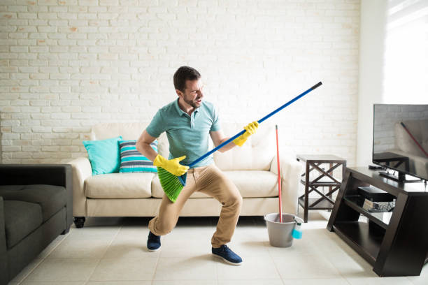 Man having fun doing house chores Attractive man having fun pretending to be playing a guitar with the broom in the living room air guitar stock pictures, royalty-free photos & images