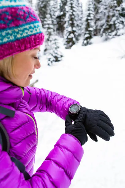Woman hiker checking the elevation on sports watch, smartwatch with altimeter app in winter woods and mountains. Girl trekker in white snowy forest trekking with electronics equipment technology.