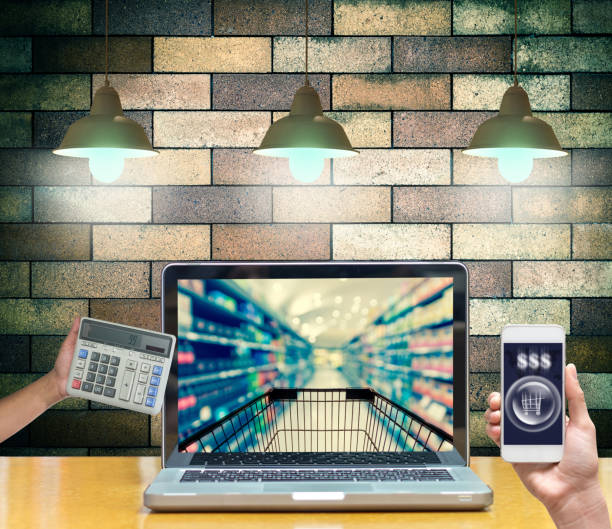 Computer notebook with hand holding smart mobile and calculator on brick wall show Abstract blurred photo of store bokeh background, online shopping concept Computer notebook with hand holding smart mobile and calculator on brick wall show Abstract blurred photo of store bokeh background, online shopping concept mark goodson screening room stock pictures, royalty-free photos & images