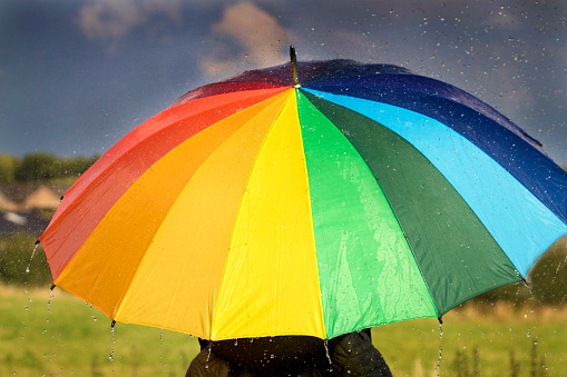 A person with rainbow colored umbrella under storm clouds close up image