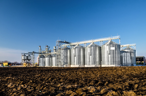 The complex silo installations for the storage of grain standing in the plowed field on a background of blue sky in winter