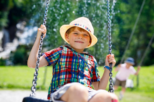 Funny kid boy having fun with chain swing on outdoor playground during rain. child swinging on warm rainy summer day. Active leisure with kids. Happy crying boy with rain drops on face