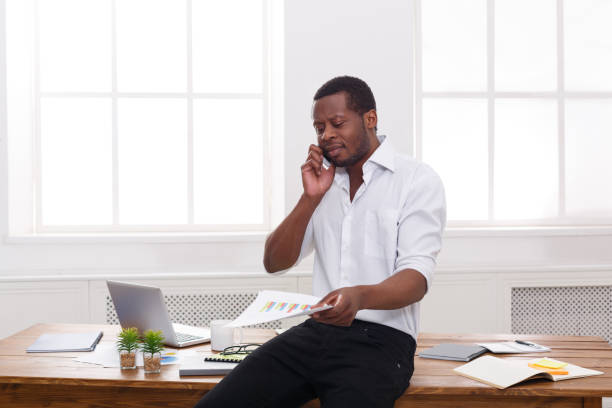 istock Young black businessman read documents and talk on mobile in modern white office 843276882