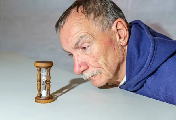 Senior man watching a time slip away as sand falls through an hourglass