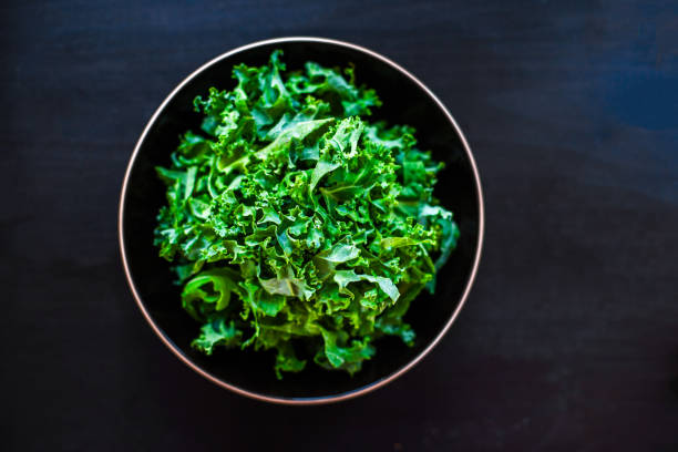 Fresh green kale salad leaves in a bowl on black board with copy space for text background\