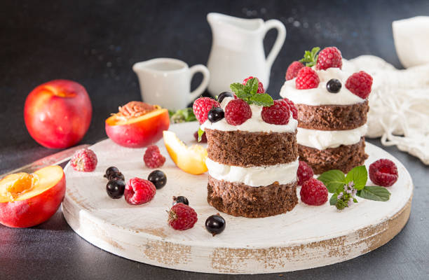 chocolate cake decorated with raspberry, black currant, wipped cream and mint on white wooden board. t - wipped cream imagens e fotografias de stock