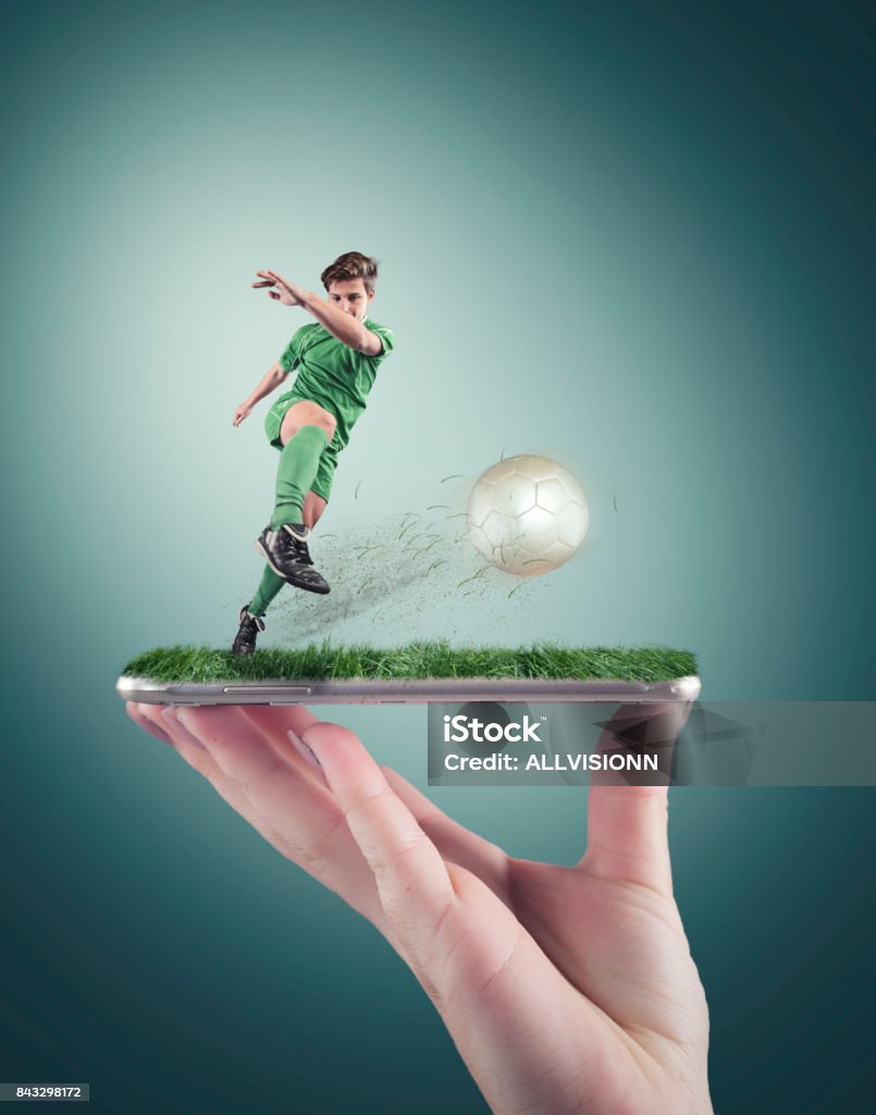 Hand holding a smartphone Hand holding a smartphone which displays a soccer match on the touch screen. Soccer player shooting the ball. Soccer Stock Photo