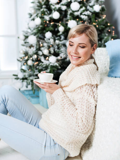 istock Young woman drinking coffee by the Christmas tree 843308954