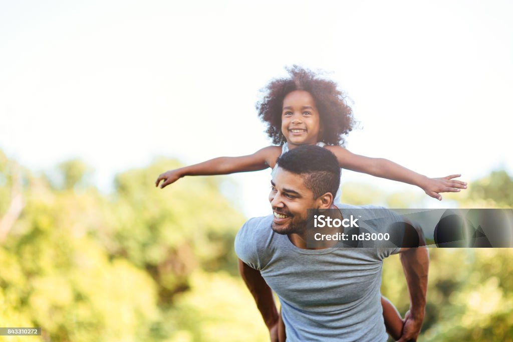 Portrait of young father carrying his daughter on his back Portrait of young father carrying his daughter on his back in nature Family Stock Photo