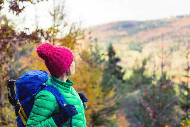 Hiking woman with backpack looking at inspirational autumn mountains. Fitness travel and healthy lifestyle outdoors in fall season nature. Female backpacker tourist walking and looking around.