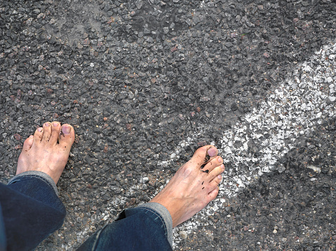Man walking on asphalt road with bare feet, above cropped view