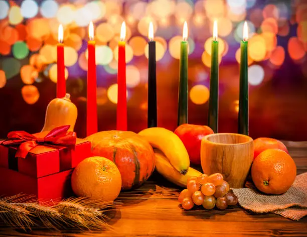 Photo of Kwanzaa holiday concept with decorate seven candles red, black and green, gift box, pumpkin, bowl and fruit on light blur bokeh background