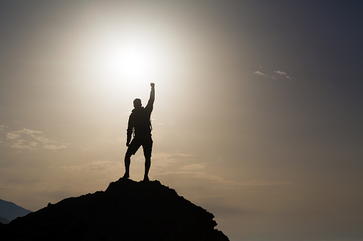 Man success with arms outstretched celebrating or praying in beautiful inspiring mountains sunrise, silhouette. Man hiking or climbing with hands up enjoy inspirational landscape on rocky Crete.