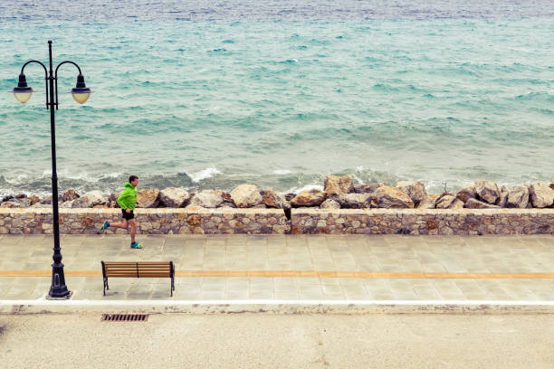 Man running on city street at seaside. Young athlete male training and doing workout outdoors in urban scene. Sport and fitness training inspiration and motivation. Vintage tone.