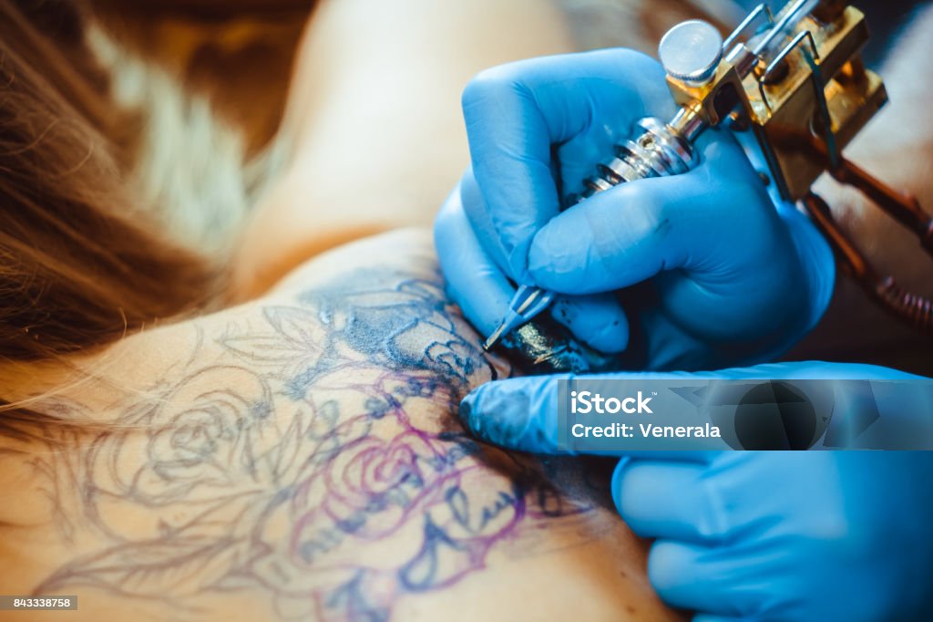 master tattoo woman on her back tattooer showing process of making a tattoo, hands holding a tatoo machine Tattoo Stock Photo