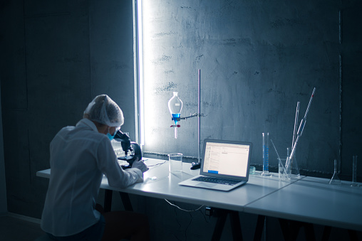 Rear view of a female scientist in a laboratory working with a microscope.