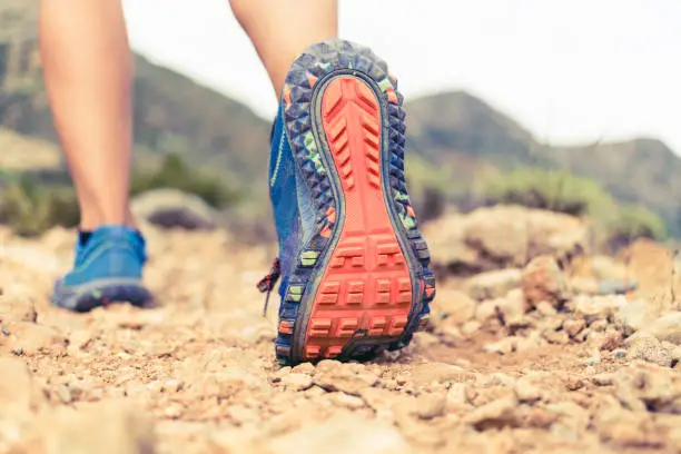 Hiking or running woman in beautiful mountains inspirational landscape. Sole of sports shoe and legs on rock trail. Hiker trekking or walking of footpath. Healthy fitness lifestyle outdoors.