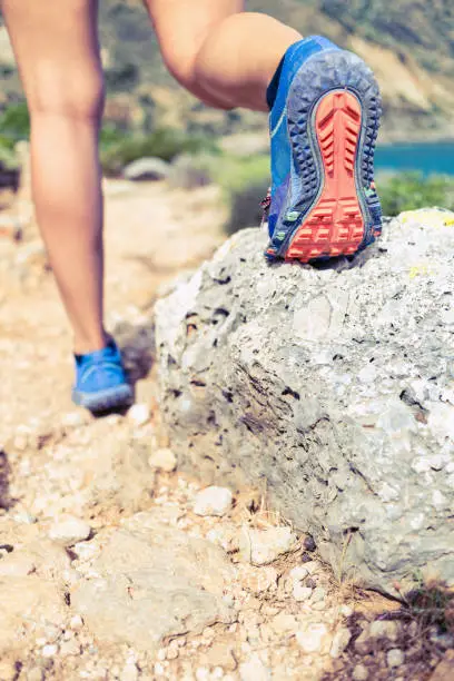 Hiking or running woman in beautiful mountains inspirational landscape. Sole of sports shoe and legs of person on rocky footpath. Hiker trekking or walking of footpath. Healthy fitness lifestyle outdoors concept.