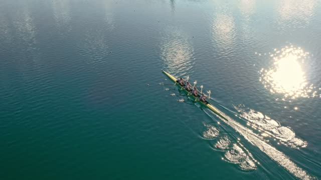 AERIAL Team of four athletes in a quad scull moving across a lake in sunshine