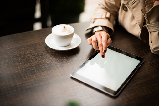 Close up of a woman using tablet while enjoying a coffee break.