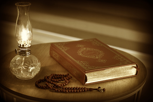 Quran, prayer beads beads and oil lamp on a wooden stand. Old, worn picture look image. Quran is holy book religion of Islam close up image