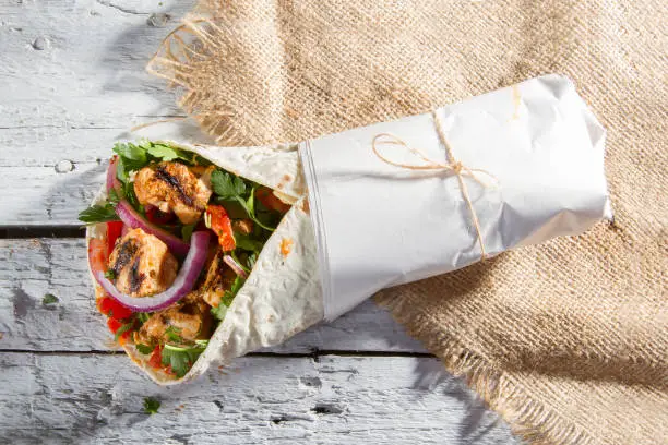 Grilled Chicken Kebab Doner Wrap with onion, parsley and tomato  on rustic white painted wood table.