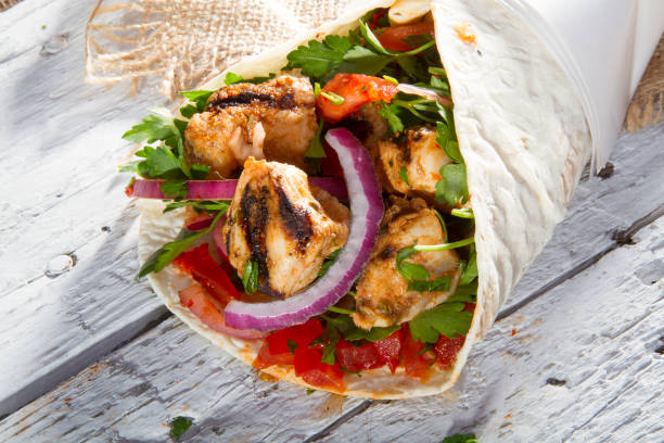 Grilled Chicken Kebab Doner Wrap with onion, parsley and tomato  on rustic white painted wood table. stock photo