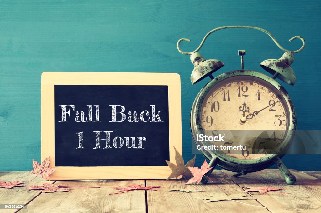 Image of autumn Time Change. Fall back concept Image of autumn Time Change. Fall back concept. Dry leaves and vintage alarm Clock on  rustic wooden table Clock Stock Photo