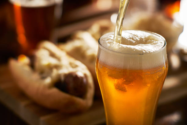 pouring amber beer into mug with bratwursts in background close up