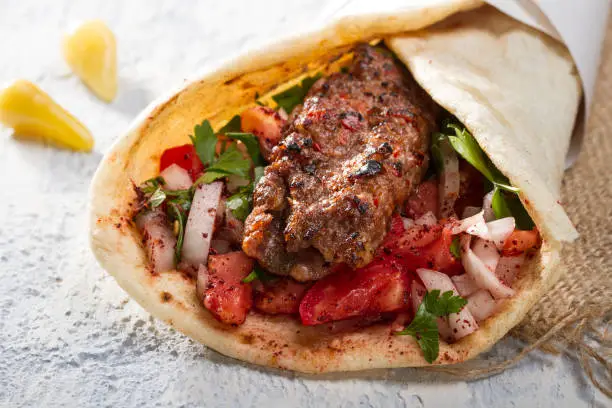 Turkish and Arabic Traditional Ramadan Adana Kebab Roll Wrap serving with yogurt, aubergine salad and hot pepper pickles on rustic wooden background.