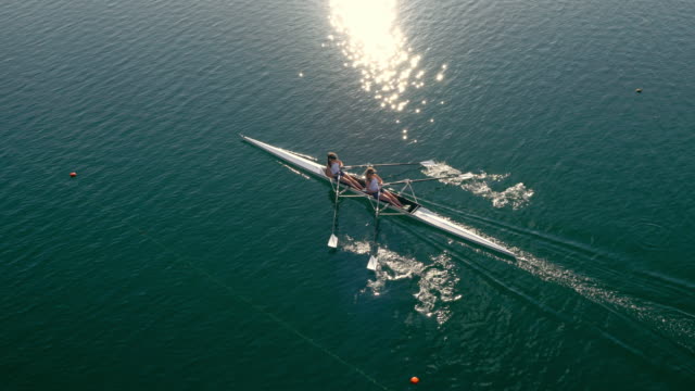 AERIAL Two rowers sculling across a sunny lake in a double scull