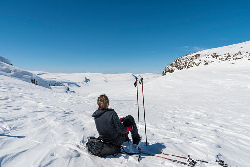 Adult male skier back country skiing. He is resting and enyojing beautiful view. Sunny day, blue sky and hills and rocks in background.  Hardangervidda National Park. Norway.